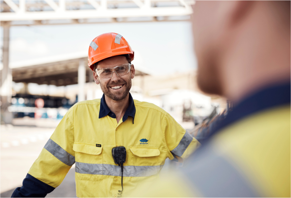 Alt Text: Two workers in PPE chatting happily outside a facility